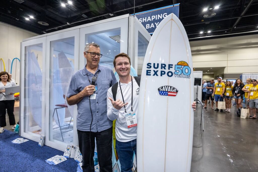 Surf Expo Show Director Roy Turner with Gunther Schwartz, who won the 50th anniversary board crafted by Savage Surfboards. Photo courtesy of Surf Expo.